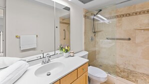 Un baño moderno con cabina de ducha de vidrio, un lavamanos blanco y un inodoro.