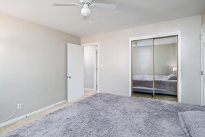 Ein Schlafzimmer mit einem Bett, einem flauschigen Teppich, einem Deckenventilator und einem Kleiderschrank mit Spiegel.