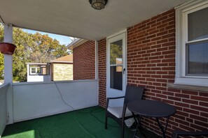 Eine überdachte Terrasse mit Backsteinmauer, Fenster, Stuhl und Tisch.