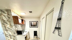 A compact kitchen with a marble backsplash, a dining area with a wooden table and chairs, and a decorative Eiffel Tower on the wall.
