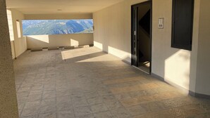 Un pasillo con suelo de baldosas, una puerta, un equipo de aire acondicionado instalado en la pared y vistas a un paisaje montañoso.