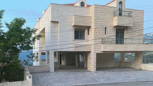 Un edificio de varios pisos con fachada de piedra, un balcón y vista al mar.