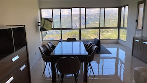 Una habitación amplia con una gran mesa de comedor, sillas, un sofá y un televisor montado en la pared.