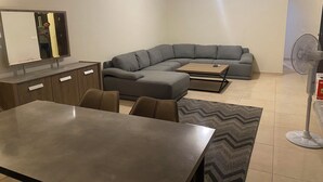 Una sala de estar moderna con un sofá modular, una mesa de comedor y un ventilador de pie.