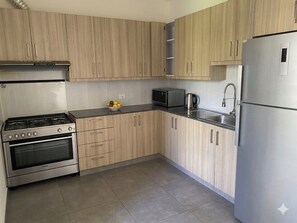 A kitchen with light wood cabinets, stainless steel appliances, and a tiled floor.