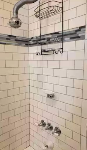 A corner of a bathroom with white subway tiles, a showerhead, and a towel rack.