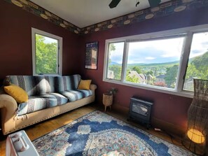 Ein gemütliches Zimmer mit einer Couch, einem gemusterten Teppich, einem Kamin und großen Fenstern mit Blick auf Grünflächen.
