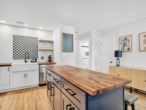 A modern kitchen with white cabinetry, a wooden countertop, and a checkered backsplash.