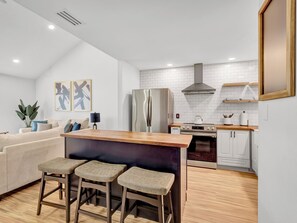 A modern kitchen with a wooden bar stool area, white cabinetry, and a stainless steel refrigerator.