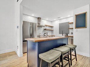 Une cuisine moderne dotée d’un réfrigérateur en acier inoxydable, d’un plan de travail en bois et de tabourets de bar.