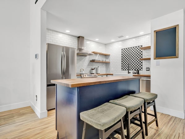 A modern kitchen with a stainless steel refrigerator, wooden countertop, and bar stools.