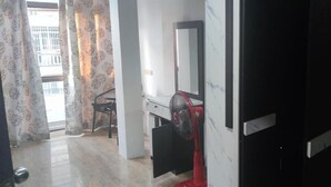 A hotel room with a bed, a desk, a chair, a fan, and a window with curtains. - Old Town (Pattaya)