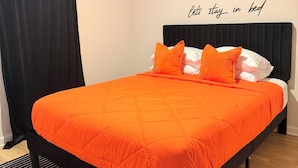En seng med et orange sengetæppe, sort sengegavl og en stribet måtte i sort og hvid.