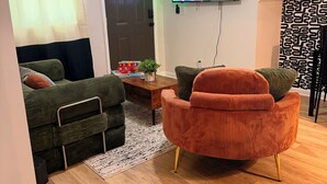 En moderne stue med en sofa, en rød lænestol, et fladskærms-tv og en loftventilator.