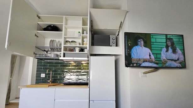 A compact kitchen with white cabinetry, a green-tiled backsplash, and a television displaying a show. - Apartment in Regla area, 1 bedroom, capacity for 4 people. (Chipiona)