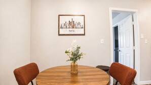 A dining area with a round wooden table, two brown chairs, a vase with flowers, and a framed cityscape picture on the wall. - 1bd, 1ba WORLD CUP Stay, Close to stadiums, Six Flags and UTA (Arlington)