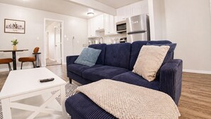 A living room with a sofa, a coffee table, and a kitchen area in the background. - 1bd, 1ba WORLD CUP Stay, Close to stadiums, Six Flags and UTA (Arlington)