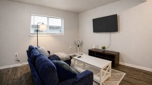 A living room with a sofa, a coffee table, a TV, a lamp, and a fan. - 1bd, 1ba WORLD CUP Stay, Close to stadiums, Six Flags and UTA (Arlington)
