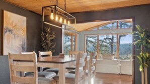 Zona pranzo con tavolo e sedie in legno, lampadario a sospensione e ampia finestra vista alberi.