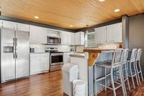 A modern kitchen with white cabinets, stainless steel appliances, a wooden ceiling, and bar stools. - Bella Vista MTB Escape • Large Patios Steps from Bike Trails (Bella Vista)