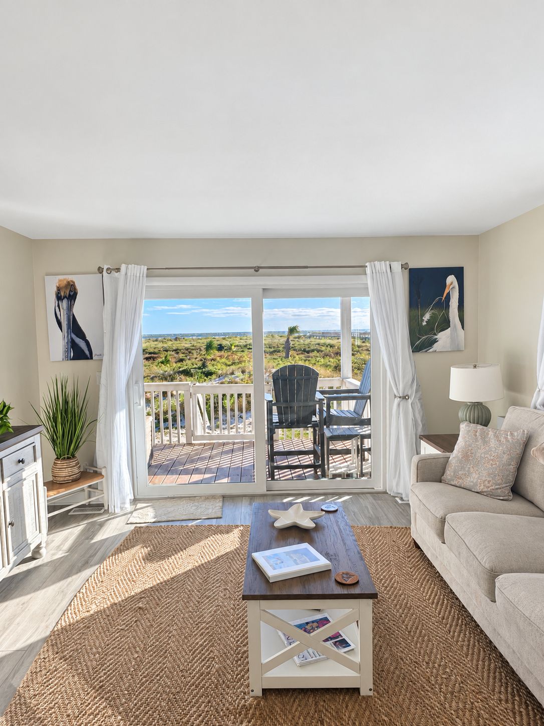 A room with a view of a beach, a sofa, a coffee table, and a dining area with chairs.