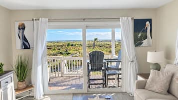 A room with a view of a beach, a sofa, a coffee table, and a dining area with chairs.
