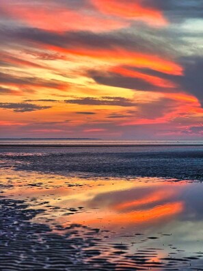 A beach with a sunset and calm water reflecting the sky.
