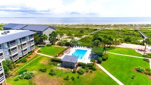 A hotel with a swimming pool, a beach view, and a parking area.