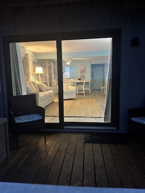 A room with a sliding glass door leading to a living area with a sofa, chairs, and a dining table.