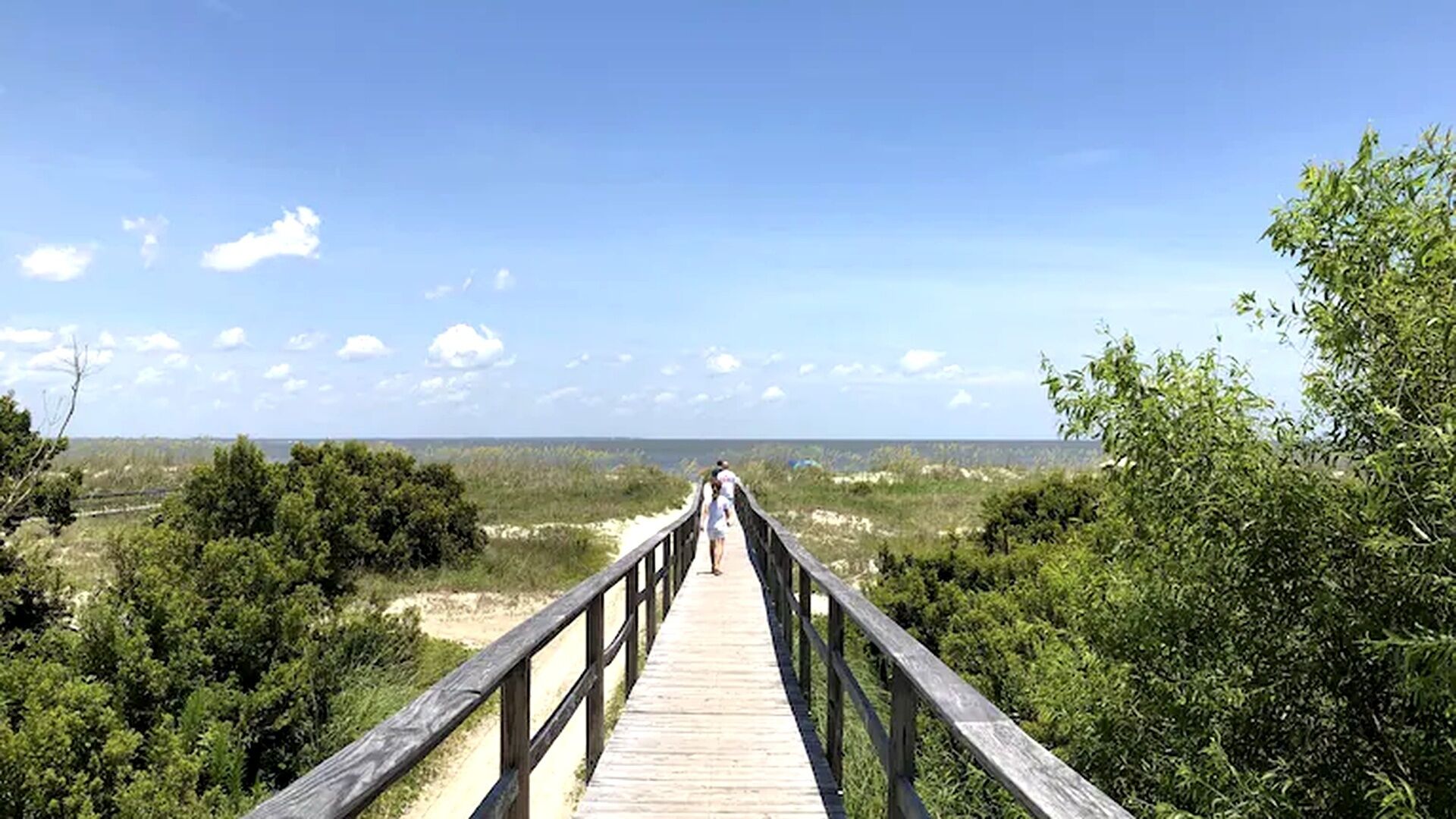 A wooden boardwalk leading to a beach with a clear sky.