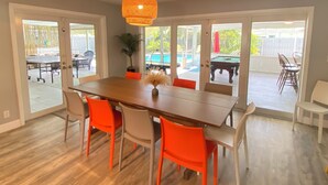 A dining area with a wooden table, orange chairs, and a hanging light fixture. - Large Private Villa with Pool, Sauna, Billiards, Minutes from the Beach (Dania Beach)