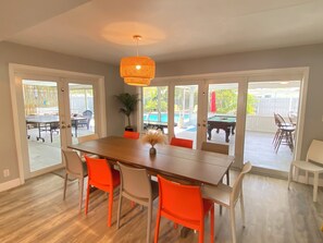 A dining area with a wooden table, orange chairs, and a hanging light fixture. - Large Private Villa with Pool, Sauna, Billiards, Minutes from the Beach (Dania Beach)