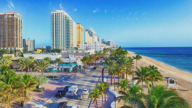 A coastal cityscape with high-rise buildings, a beach, and a parking area with palm trees. - Large Private Villa with Pool, Sauna, Billiards, Minutes from the Beach (Dania Beach)