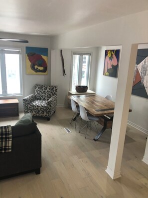 Un salon moderne avec un canapé à motifs, une table à manger avec des chaises et des œuvres d’art accrochées aux murs.