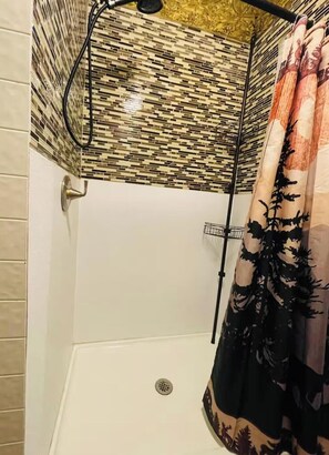 Una doccia con parete rivestita in piastrelle, soffione metallico e tenda a motivi floreali.
