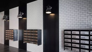Eine moderne Lobby mit Backsteinwand, schwarzen Bodenfliesen und einer Reihe von Postfächern mit Zimmernummern.