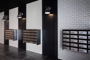 A modern lobby with a brick wall, black floor tiles, and a row of mailboxes with room numbers. - Stylish city retreat, coffee machine, balcony and city views and free carpark! (Auckland)