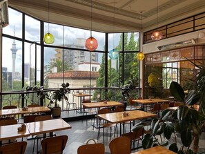 A restaurant with large windows, wooden tables, and hanging pendant lights. - Stylish city retreat, coffee machine, balcony and city views and free carpark! (Auckland)