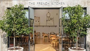 Ein Restaurant mit Eingangsbereich, ein Schild zeigt 'The French Kitchen'. Das moderne Innere zeichnet sich durch Holzkunst und Zimmerpflanzen aus.