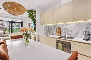 A modern kitchen with a marble backsplash, wooden cabinets, and a dining area with a large table and chairs. - Stylish city retreat, coffee machine, balcony and city views and free carpark! (Auckland)
