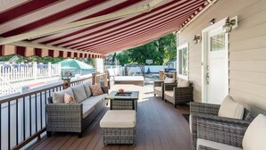 Eine überdachte Terrasse im Freien mit Korbmöbeln, einem Tisch und Blick auf Pool und Tennisplatz.