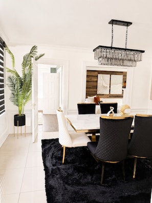 Un comedor con una mesa blanca, sillas blanco y negro, un felpudo negro y un candelabro colgante.