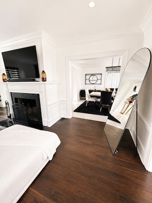 Un dormitorio moderno con chimenea, televisor, zona de comedor con alfombra negra y un espejo grande.