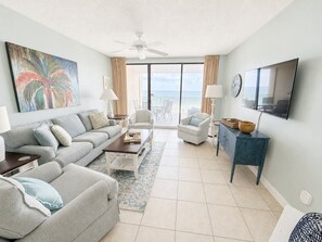 Ein Wohnzimmer mit einer Couch, Sesseln, einem Couchtisch, einem Fernseher und einem Balkon mit Blick.