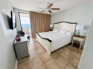 A hotel room with a bed, a desk, a television, a ceiling fan, and a view of the ocean. - Bluewater 603 - Direct Gulf Front (Orange Beach)