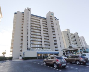 A multi-story hotel with a central entrance, parking lot, and a clear sky. - Bluewater 603 - Direct Gulf Front (Orange Beach)