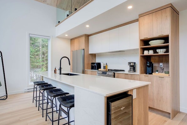 A modern kitchen with a large island, bar stools, wooden cabinets, and a view of the outdoors.