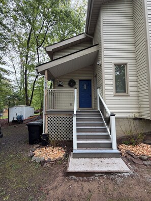 Ein zweistöckiges Haus mit Veranda, einer blauen Tür und einem kleinen Vorgarten.