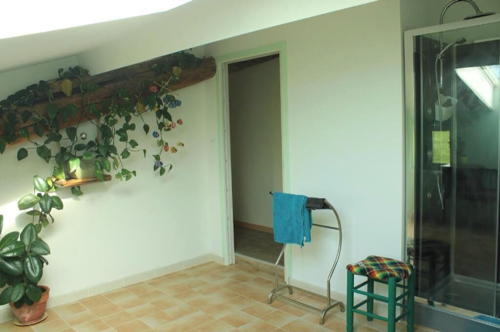 Une pièce avec un sol carrelé, un espace douche, un petit tabouret avec une serviette et des plantes en pot.