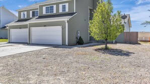 A two-story house with two attached garages, a small tree, and a gravel driveway. - Great for a group! Close and convenient! Fiber high speed internet! (Rock Springs)